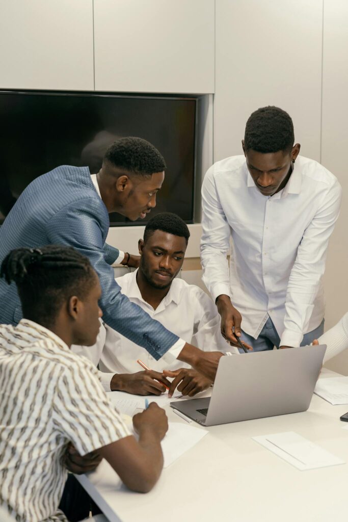 Four men collaborate on a project using a laptop in a modern office environment.
