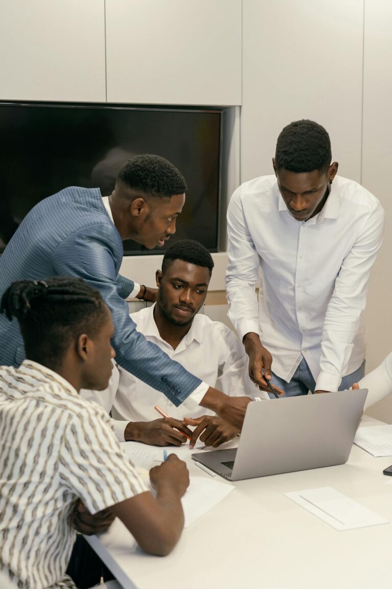 Four men collaborate on a project using a laptop in a modern office environment.