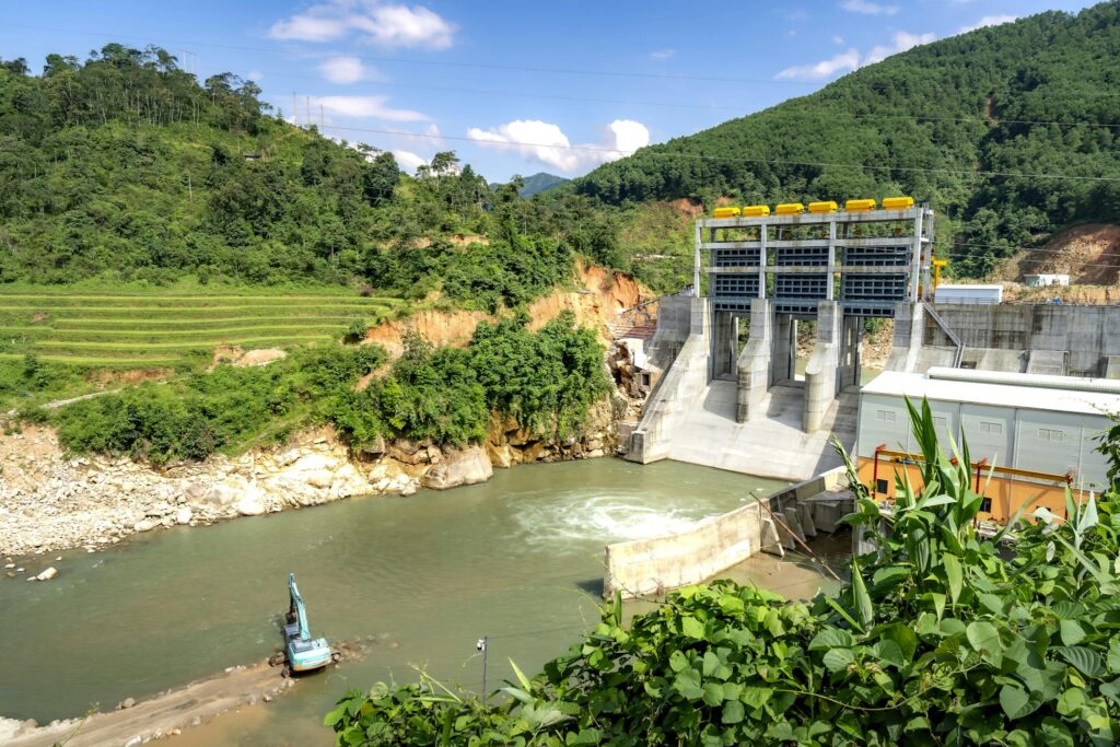 Scenic view of a hydroelectric dam nestled in a lush green valley, surrounded by hills.